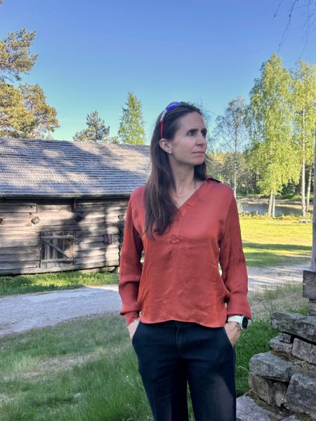 Kvinne står sidevendt foran en eldre trebygning.